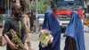 FILE - Afghan burqa-clad women walk past a Taliban security officer along a street in Jalalabad on April 30, 2023. 