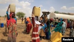 Sudanese refugee women who fled violence in Sudan's Darfur region carry jerrycans of water as they walk to their shelter near the border between Sudan and Chad in Koufroun, Chad, May 10, 2023.