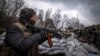 A Ukrainian serviceman holding an assault rifle looks at a Russian drone in a trench at the front line east of Kharkiv on March 31, 2022.