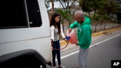 Una mujer sostiene un embudo y una manguera mientras un hombre llena su tanque después de quedarse sin gasolina en Caracas, Venezuela, el jueves 23 de marzo de 2017.