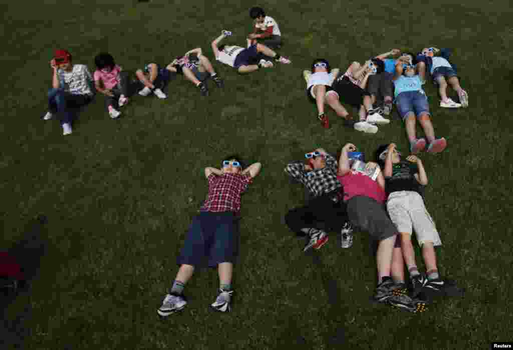 School children using solar viewers lie down on a lawn as they observe an annular eclipse at Hirai Daini Elementary School, Tokyo, Japan, May 21, 2012. Un grupo de estudiantes Hirai Daini, escuela primaria de Tokio, Jap&oacute;n, utilizan protectores para