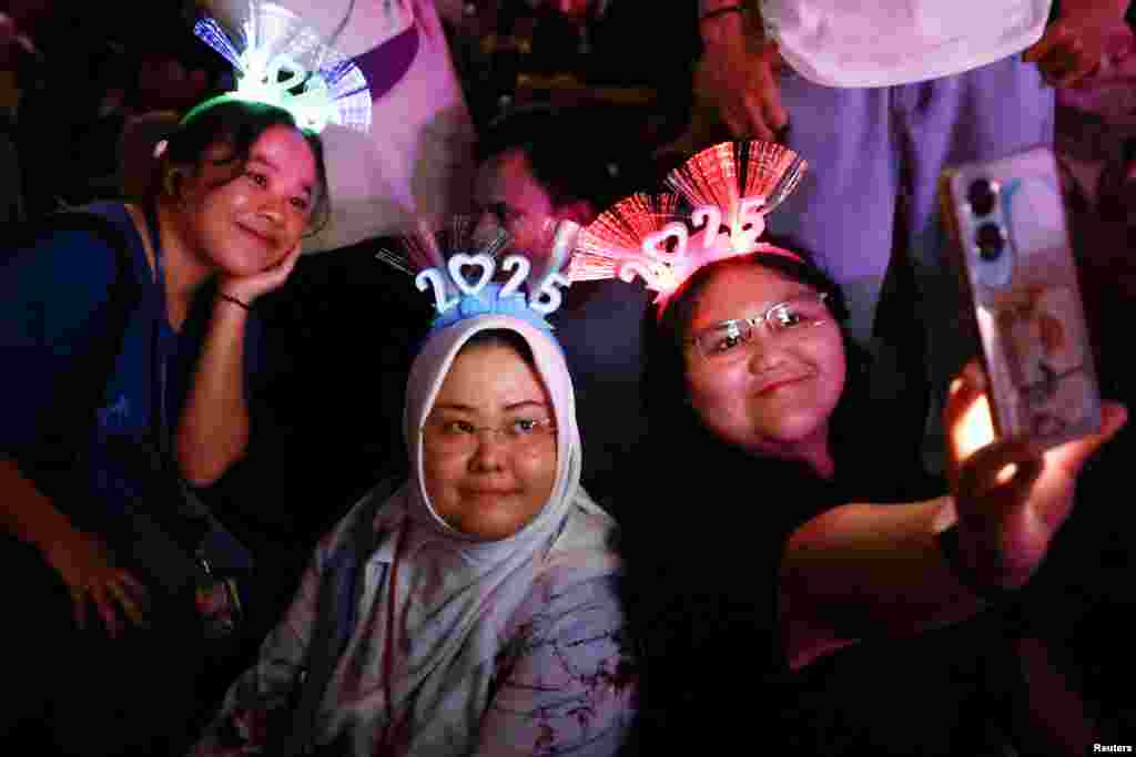 Mulheres que usam faixas &#39;2025&#39; tiram selfies durante as celebrações da véspera de Ano Novo em Jacarta, Indonésia, a 31 de dezembro de 2024.