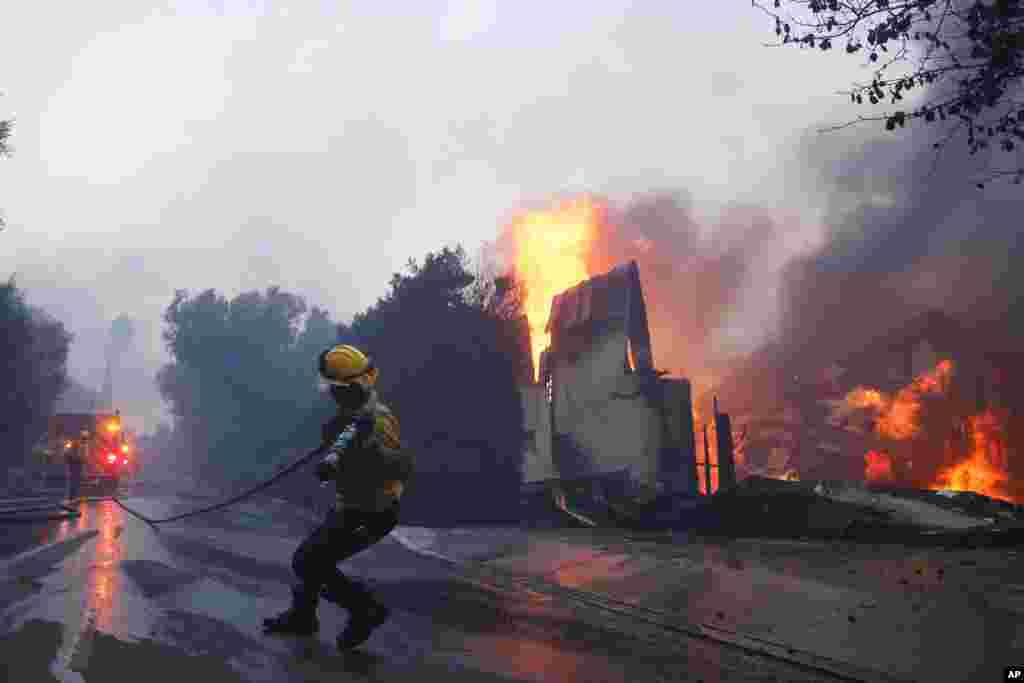 Um bombeiro luta contra o avanço do Corpo de Bombeiros de Palisades enquanto queima uma estrutura no bairro de Pacific Palisades, em Los Angeles, a 7 de janeiro de 2025.