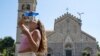 A girl pours a bottle of water on her face and head as she cools off in front of a church in the centre of Messina, on the island of Sicily, during a heat wave on July 16, 2023.